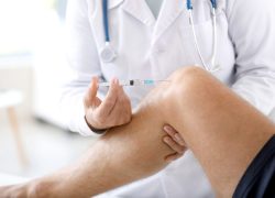 Doctor giving sportsman with joint pain injection in clinic, closeup