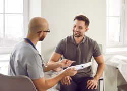 Portrait of a happy smiling young man patient in medical office listening to doctor holding report file with appointment and giving consultation during medical examination in clinic.